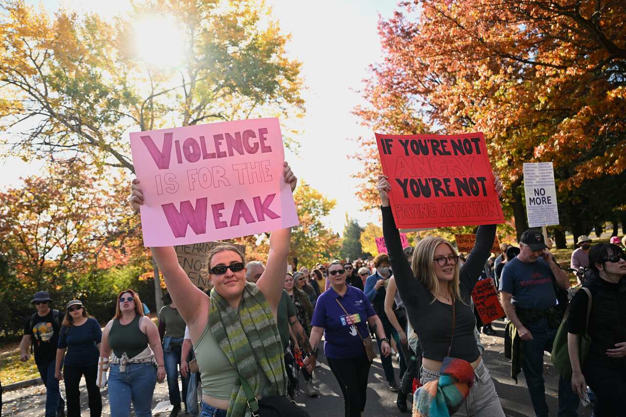 Women holding signs during a protest. One of the signs reads "Violence is for the weak"