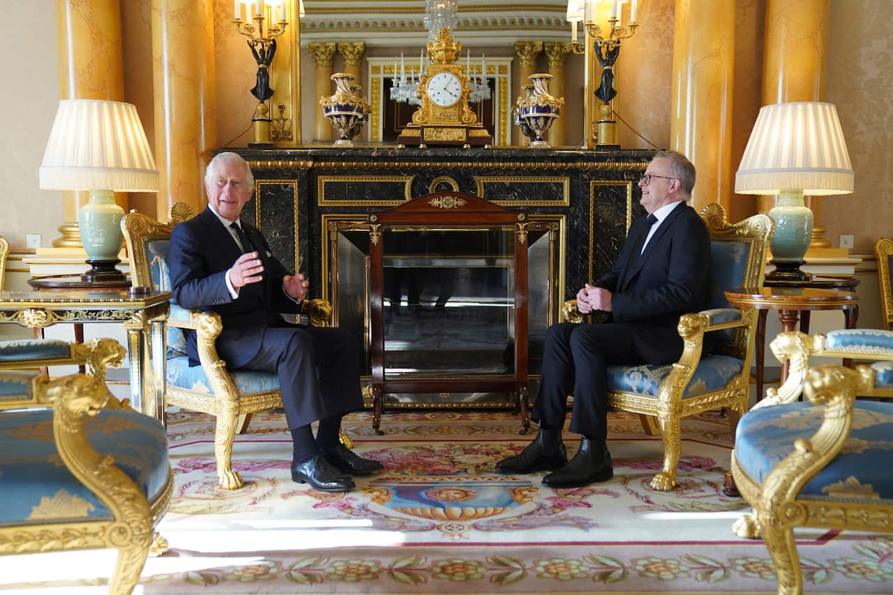Two men sit in gold chairs inside