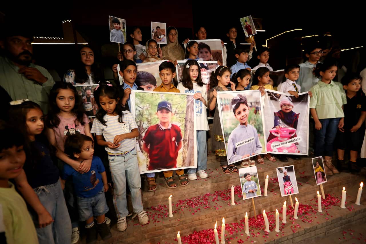 Children holding posters of men gather at a candlelight vigil.