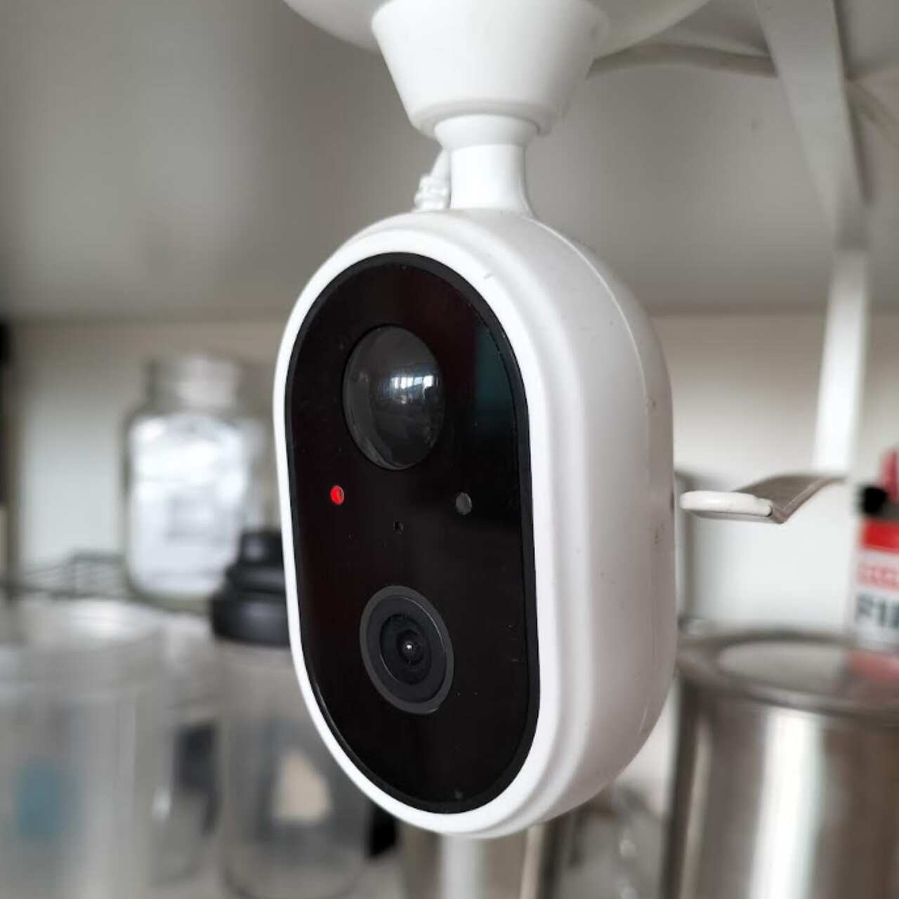 Close-up of a security camera with bottles and kitchen equipment in the background