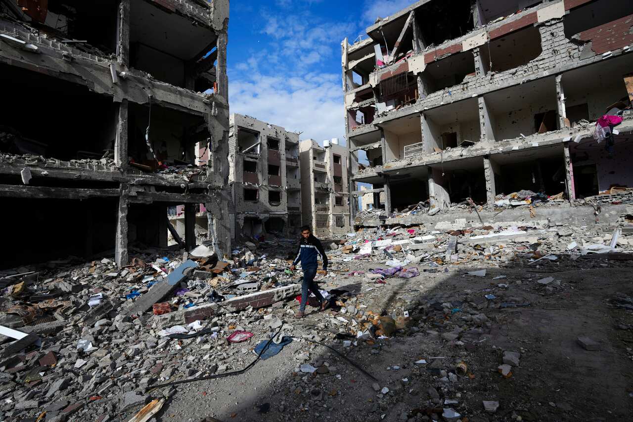 A man walking along a street strewn with debris. Destroyed buildings are around him.