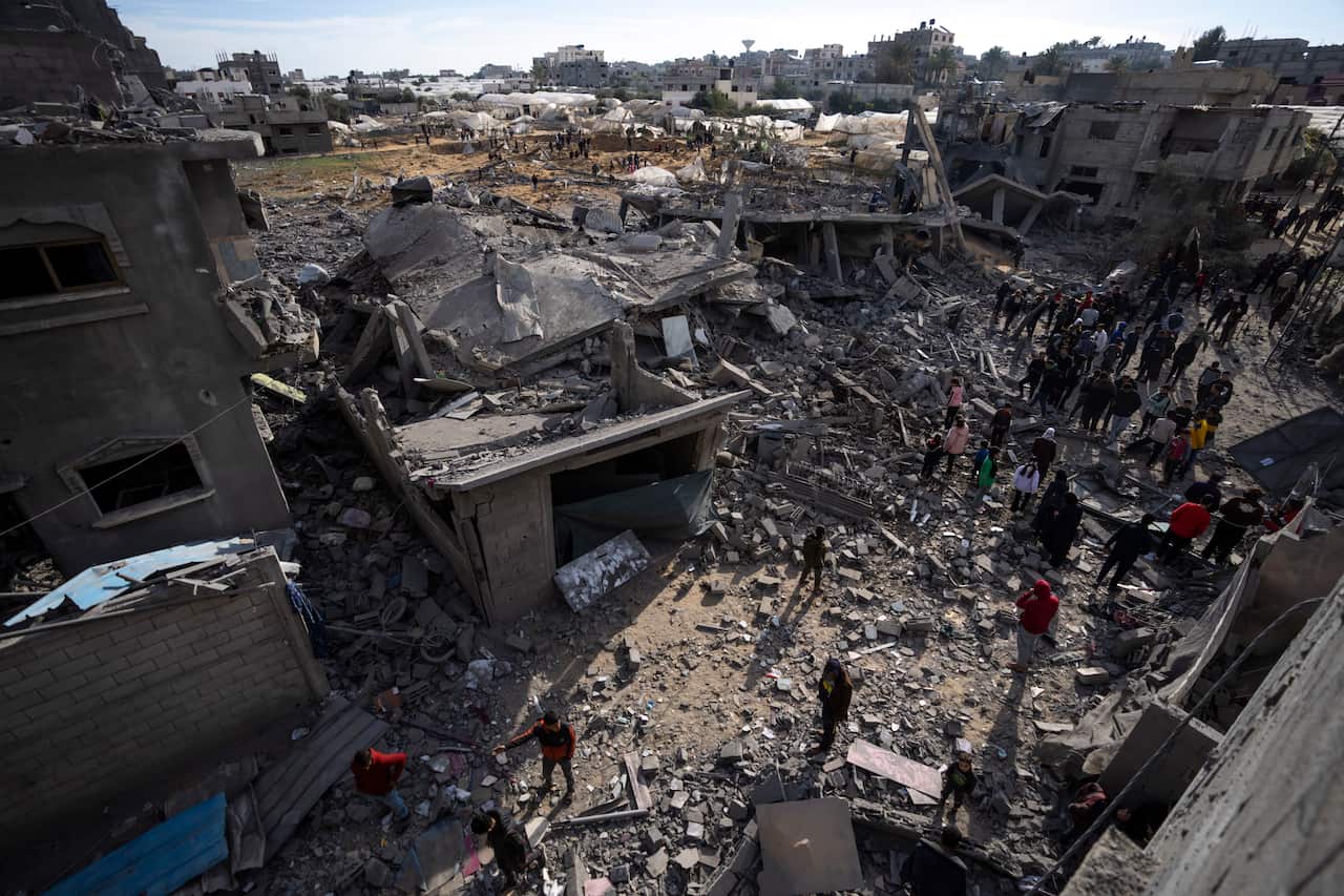 Bird's eye view of damaged buildings surrounded by rubble. People gather around the ruins.