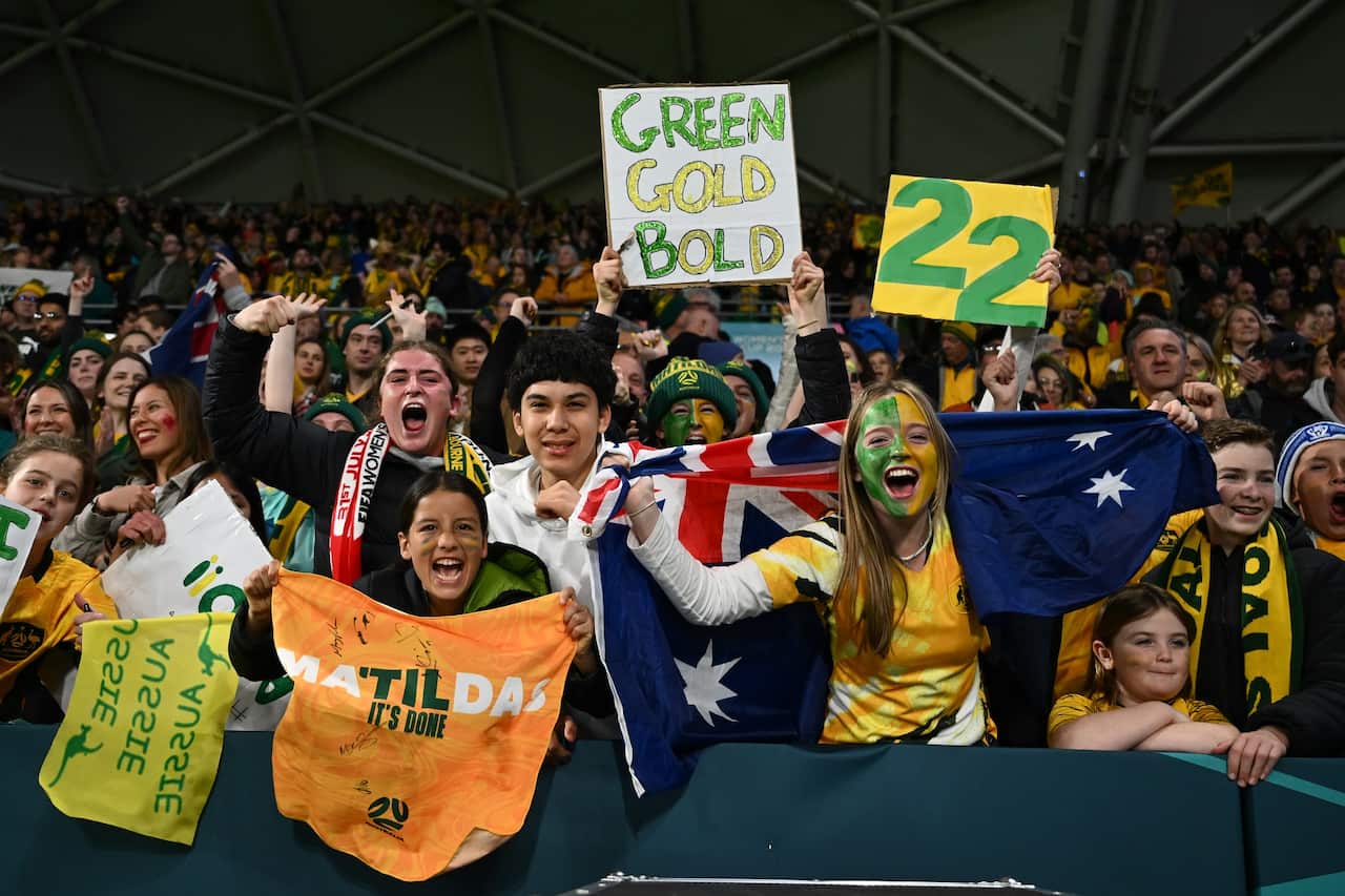 Fans of the Matildas in yellow and gold wave flags. 