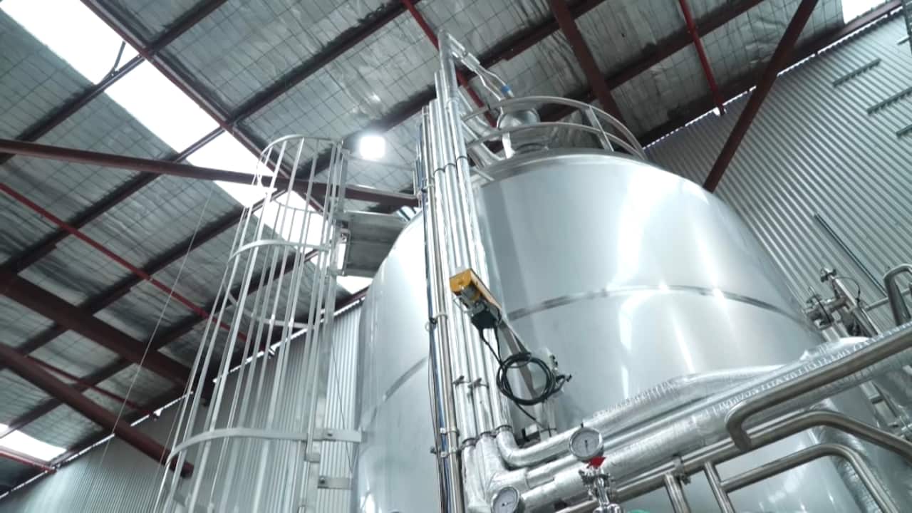 A large stainless steel tank in a factory is connected to a series of tubes.