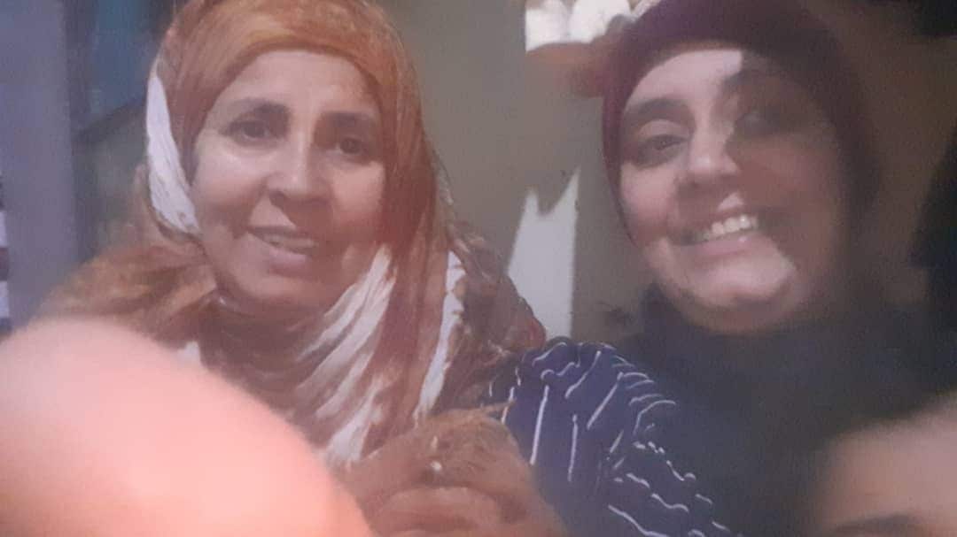 Two women, identified as Qazwan Tarbosh’s sisters, sit together and smile for a photo.