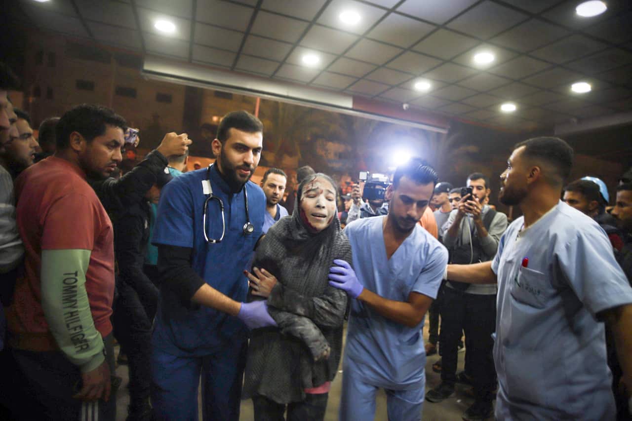 A wounded woman is helped to walk by two medical staff wearing blue uniforms. 