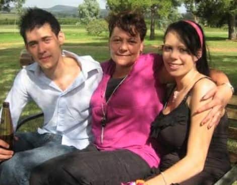 A man in a white shirt sits next to a woman in a pink shirt and another women in a black singlet top.