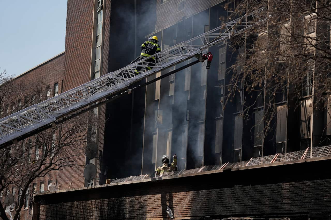 Fire Marshals inspect the scene of a deadly blaze in downtown Johannesburg. The building's exterior is blackened with soot and smoke.