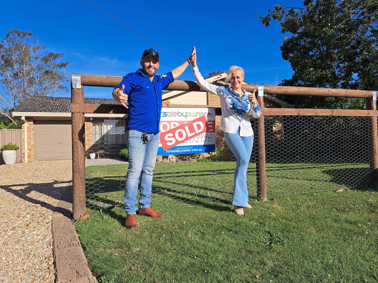 A man and woman smile as the high five in front of a "sold" sign outside a property.