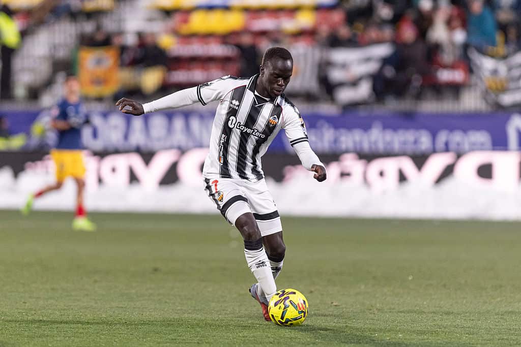 A man in a black and white striped football shirt dribbling a yellow football
