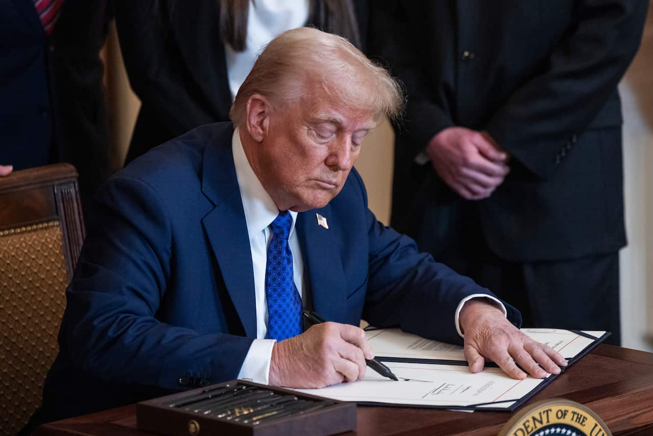 Donald Trump signs a document while sitting at a desk.