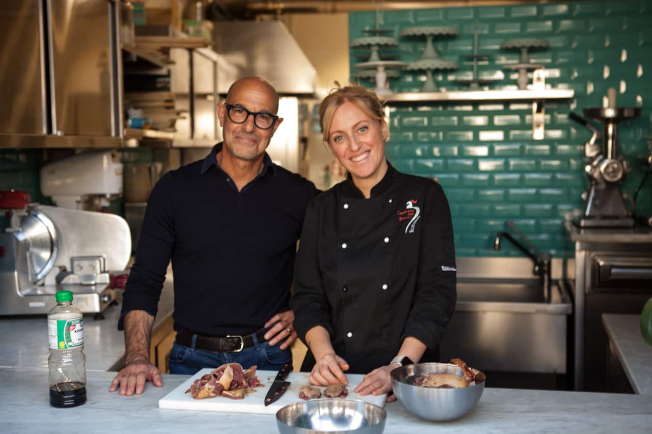 Stanley Tucci and a chef smile for the camera in a kitchen