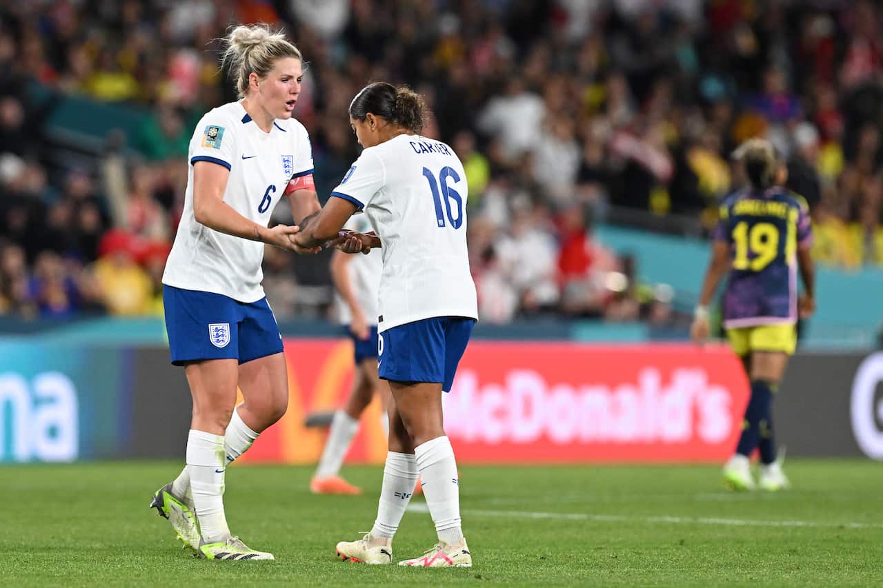 Two women in white football uniforms on the pitch.