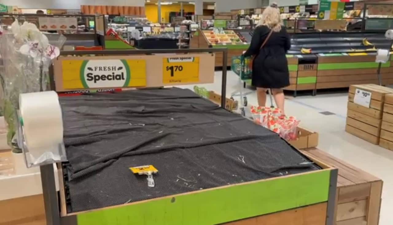 Empty shelves in a supermarket, a woman with a trolley walks past