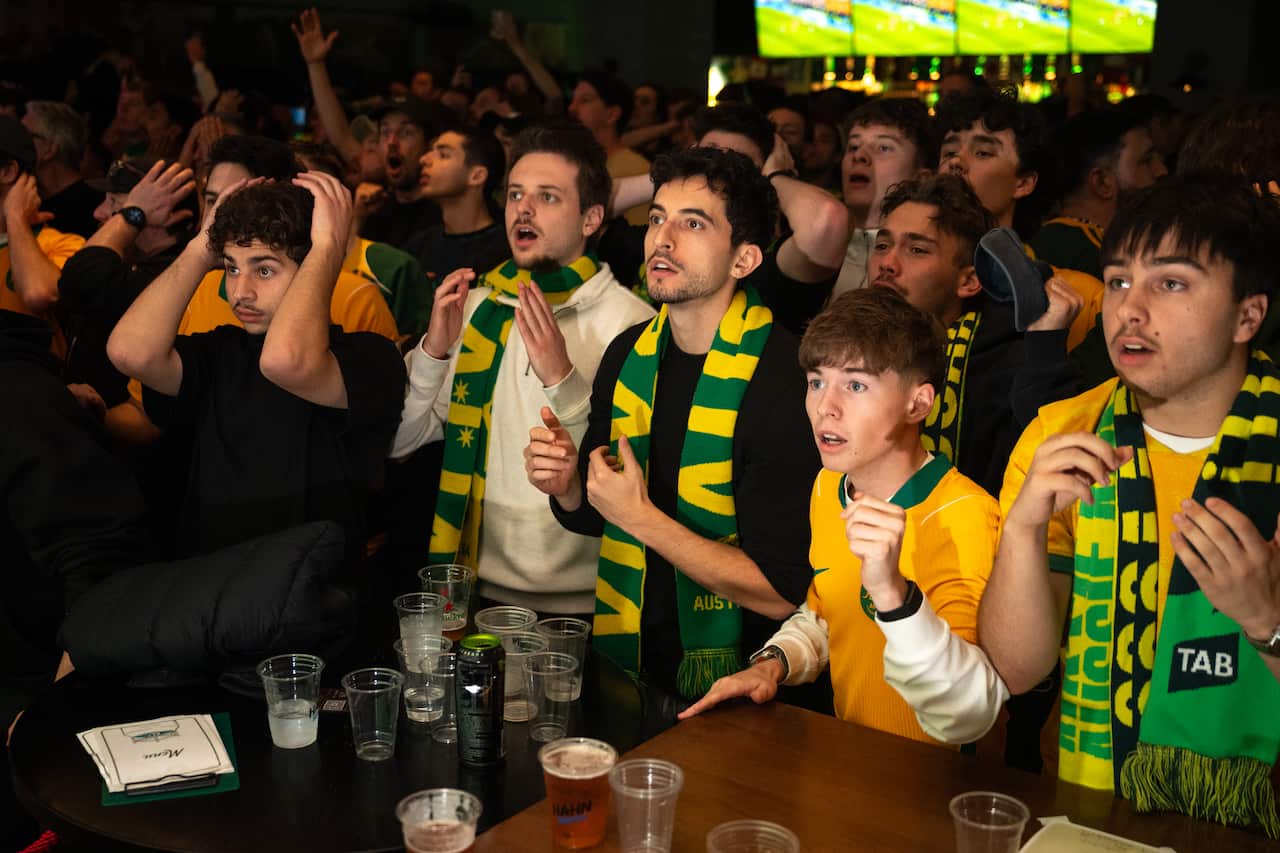 Australian football fans dressed in green and gold reacting to a play in a packed pub