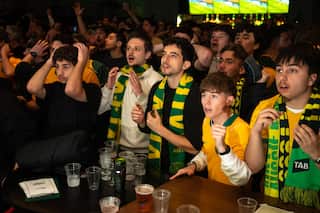 Australian football fans dressed in green and gold reacting to a play in a packed pub