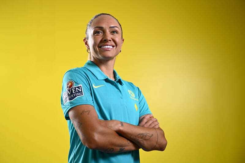 A woman in a teal polo shirt with crossed arms in front of a yellow background