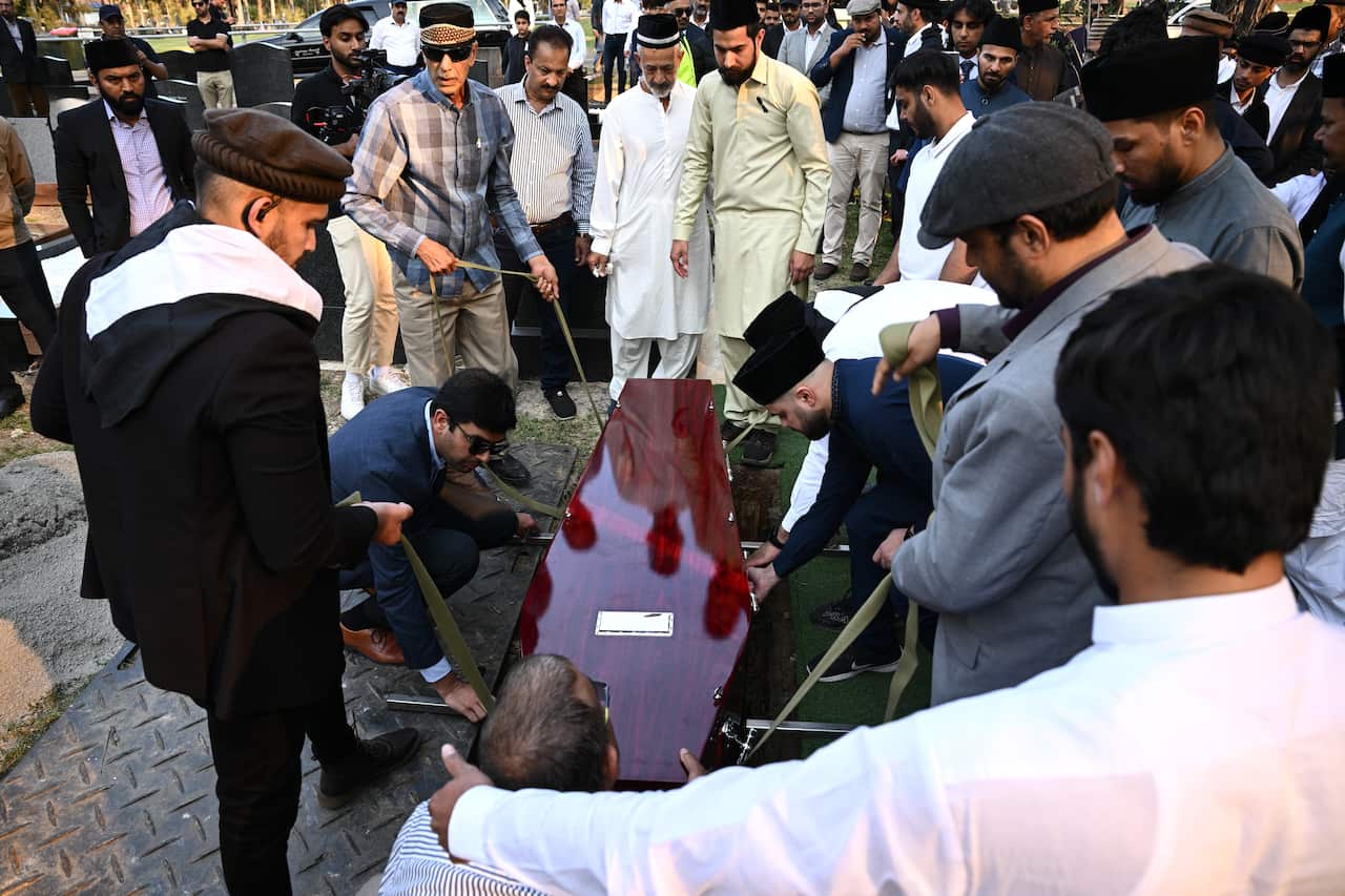 Men lower a casket at into the ground.