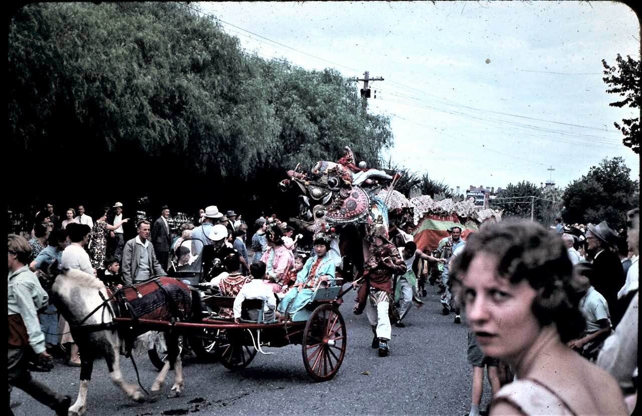A Chinese dragon dances behind a horse and carriage as a crowd watches