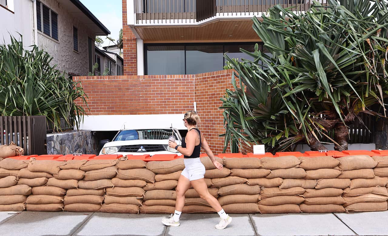 Sandbags in front of a house. A woman is walking past 