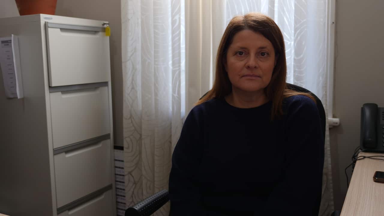 A woman in a navy jumper is sitting at a desk in an office.