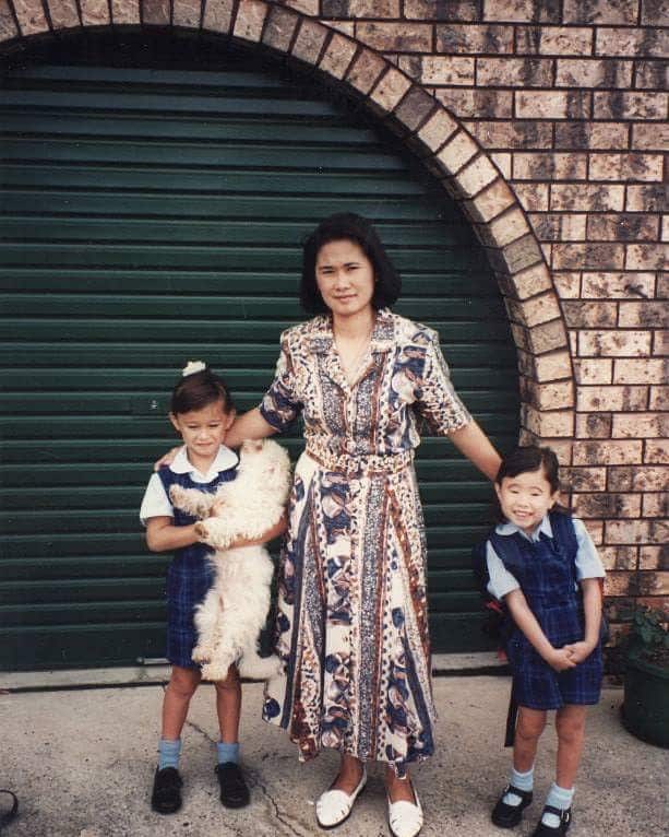 A woman stands outside a garage door with her two young children.