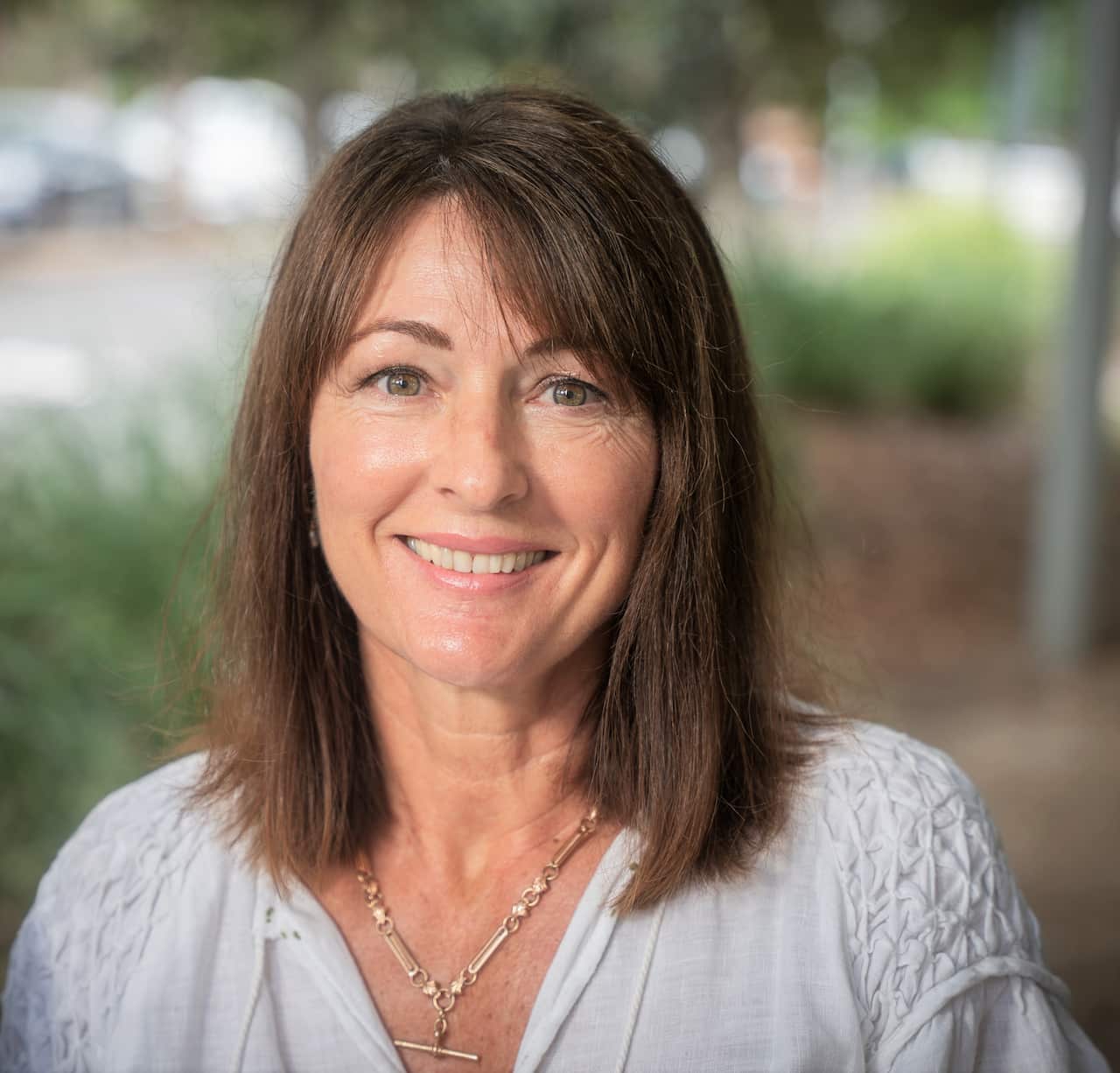 A woman in a white top, smiling and sitting in a garden