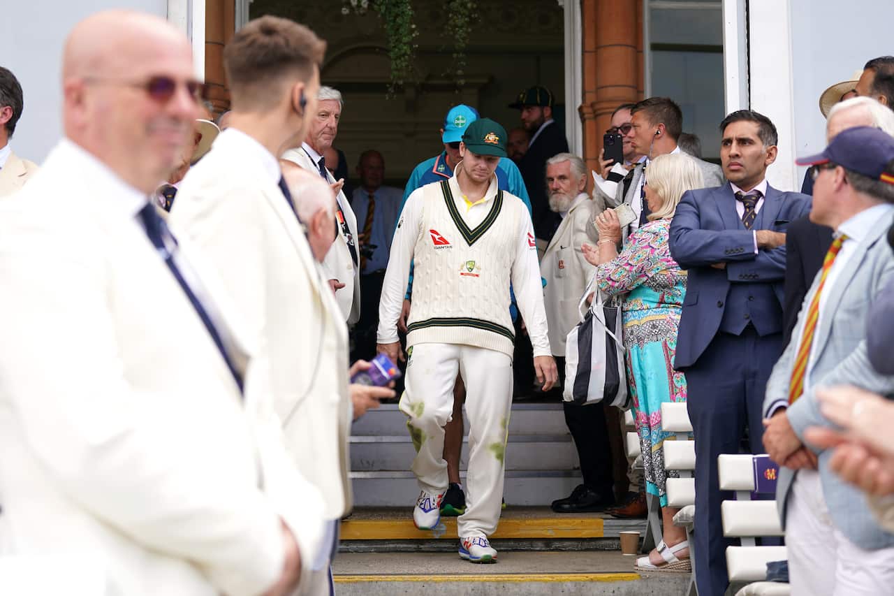 A man in cricket gear walks down the stairs as people on either side look on.