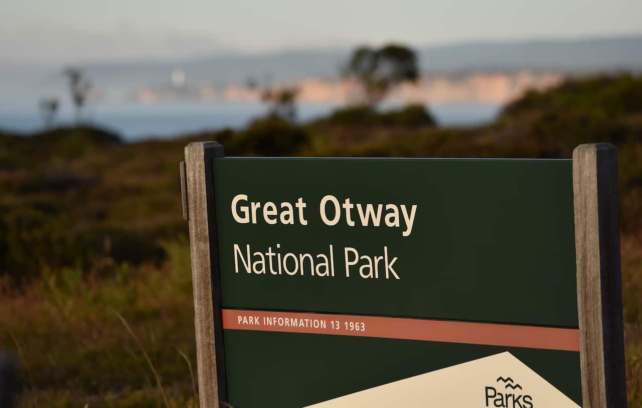 Smoke from the Otways bushfire rises over the Split Point Lighthouse in front of a Great Otway National Park sign on the Great Ocean Road