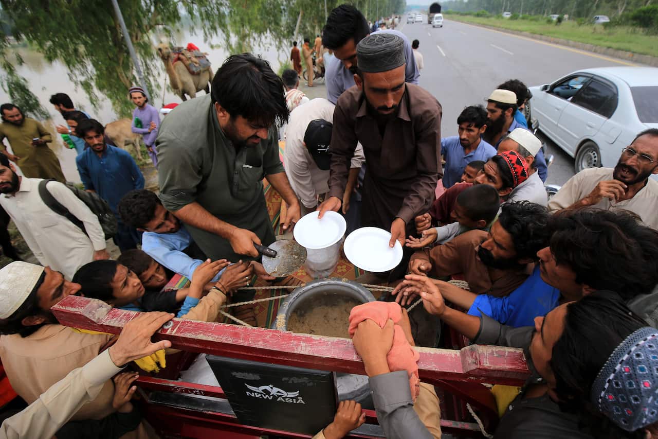 People clamber for a plate of food from a man offering plates. 
