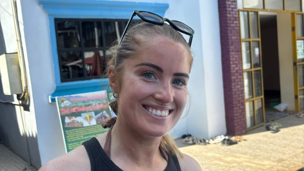 a young blonde woman smiling out the front of a blue hostel