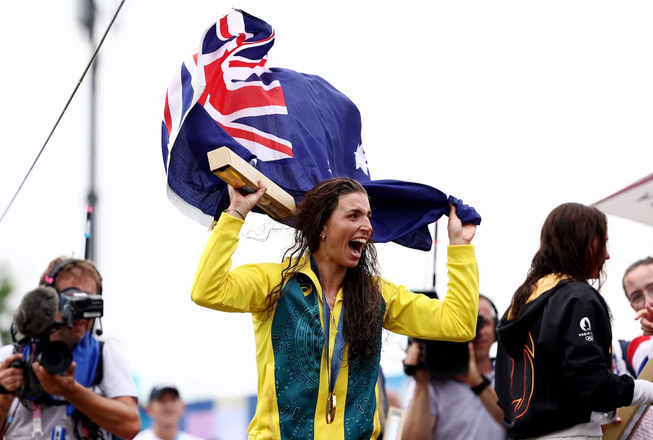 Jessica Fox, wearing a green and gold tracksuit top and with a gold medal around her neck, waves an Australian flag above her head