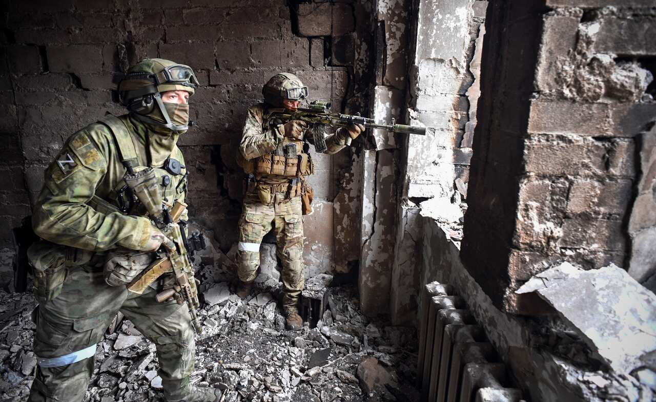 Two soldiers standing at the window of a damaged building holding guns.