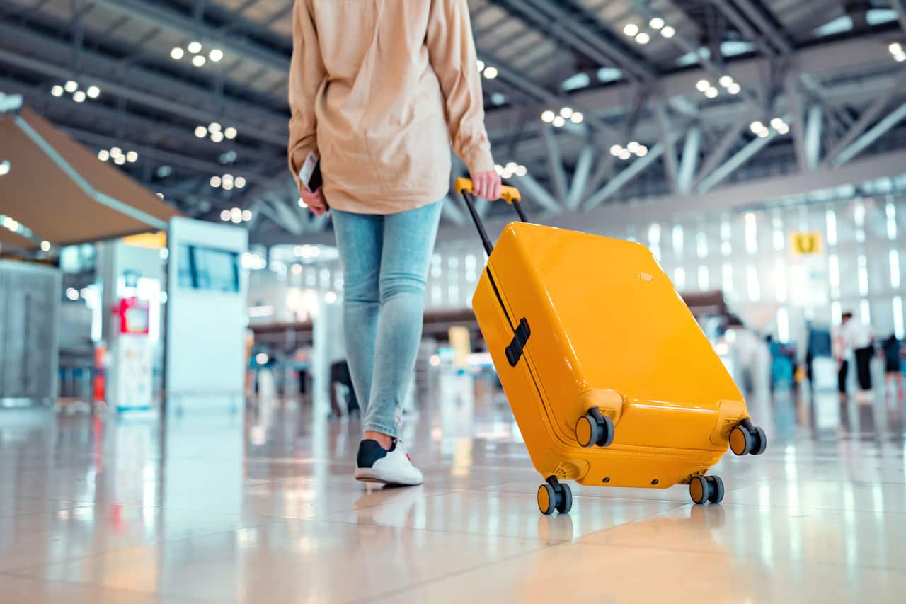 Woman walking with a yellow suitcase through an airport terminal.