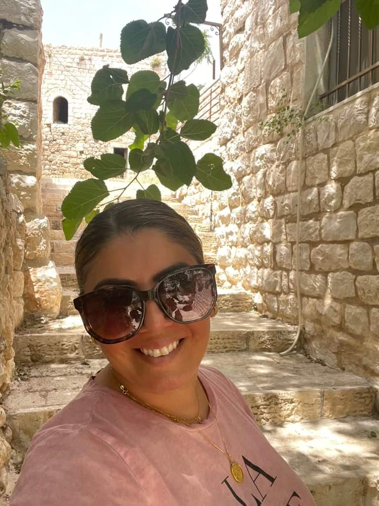 A woman wearing sunglasses smiling in front of a white brick wall
