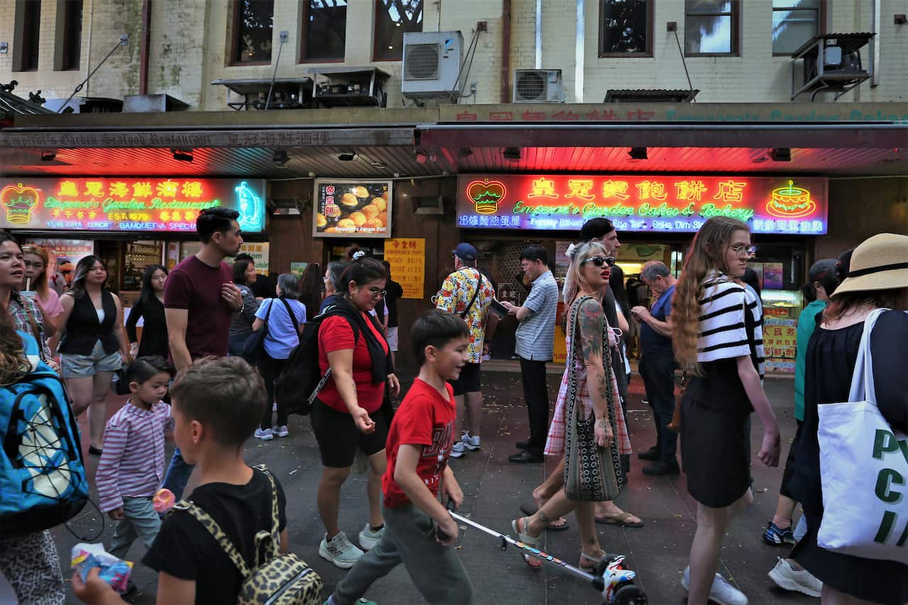 Lots of people walk past restaurants with neon signs in Sydney's Chinatown district.