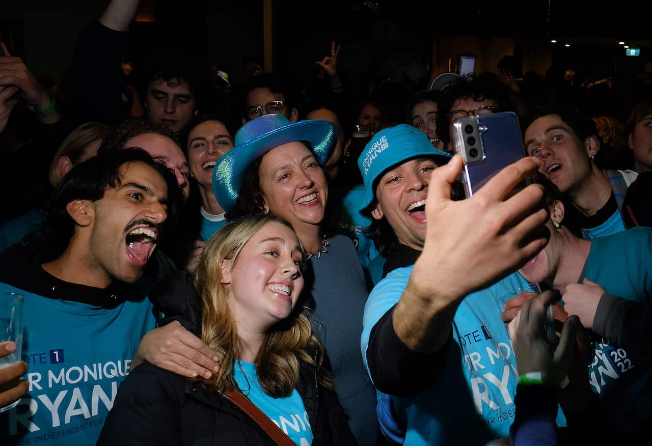 A woman poses for a selfie with a crowd wearing Monique Ryan T-shirts