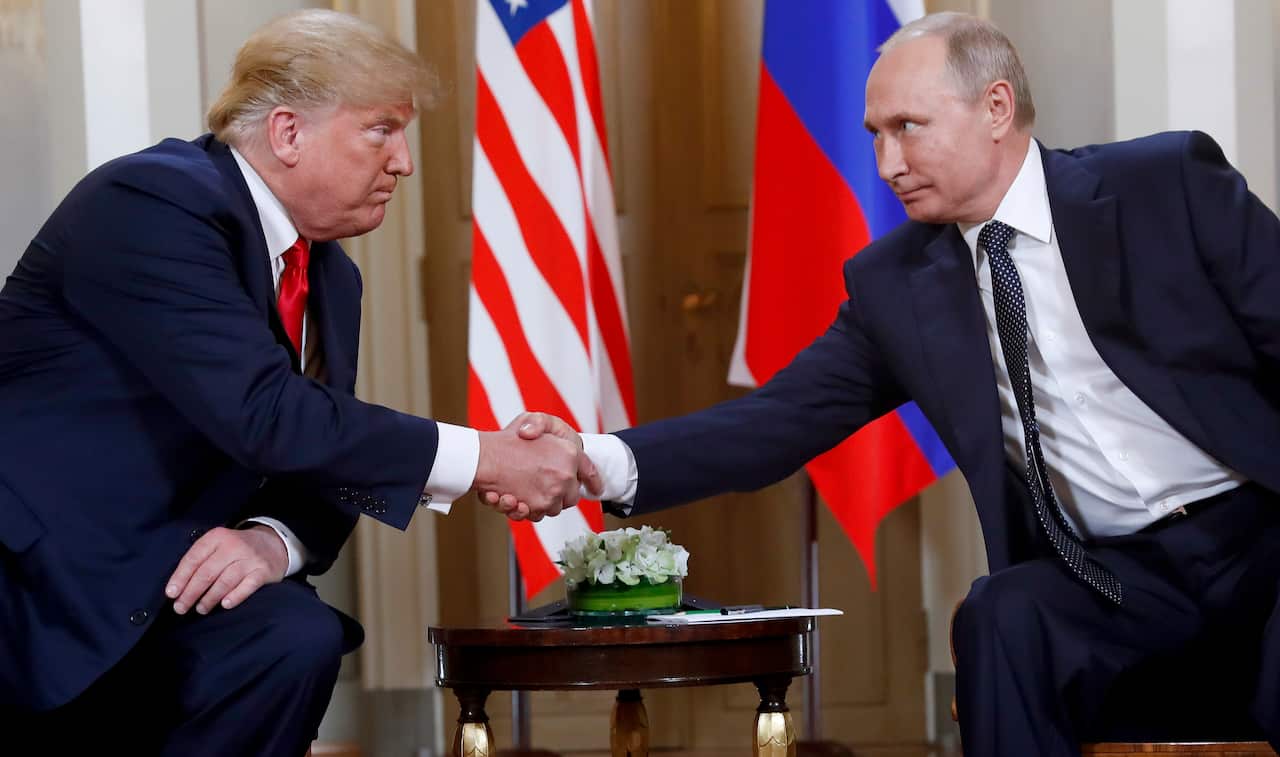 Donald Trump and Vladimir Putin, both sitting down, shake hands.