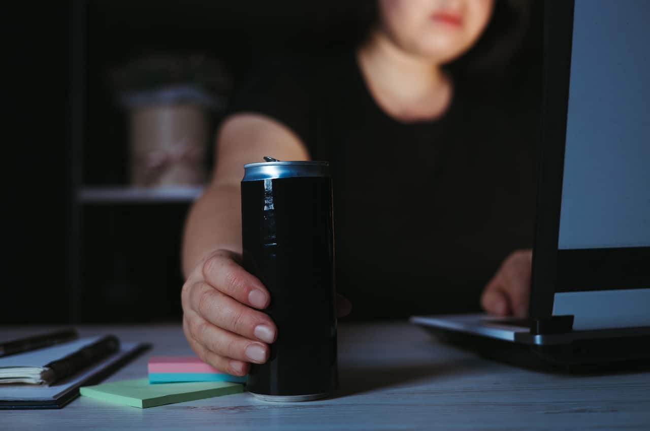 A woman at a laptop holding a can of energy drink