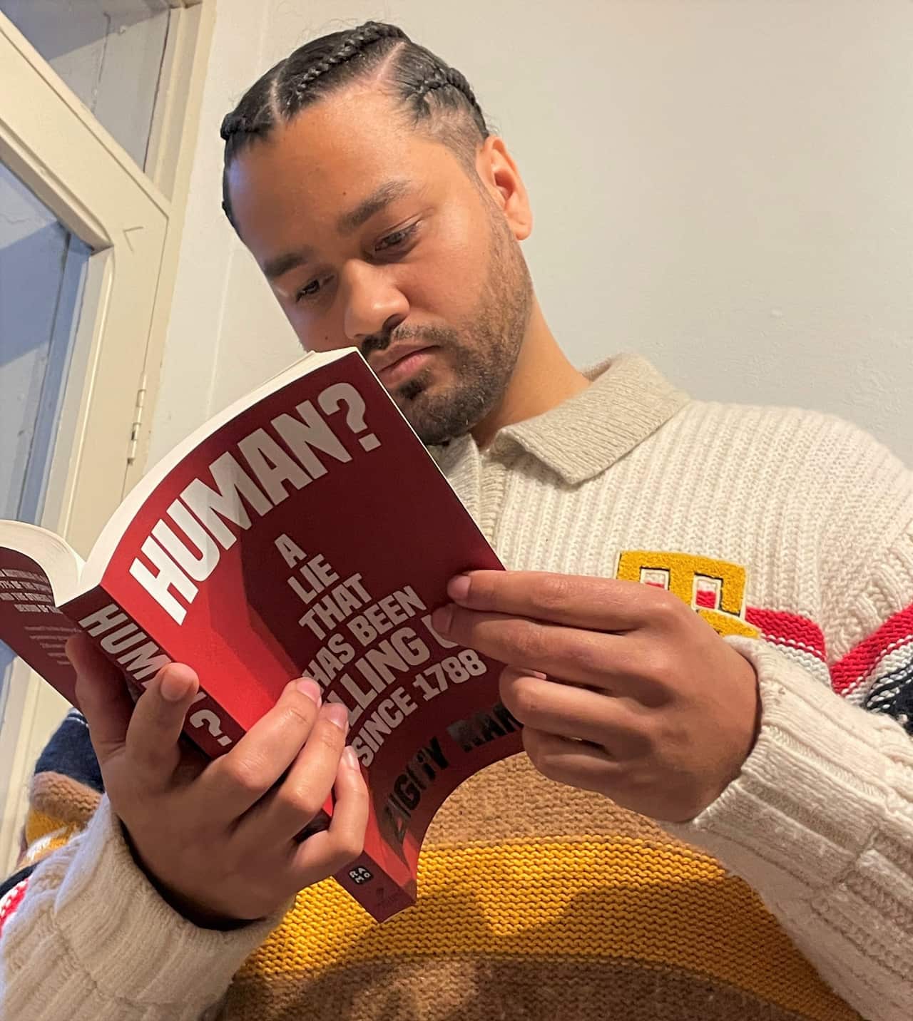 A man in a jumper looks at a book he is holding open. The book is titled Human?
