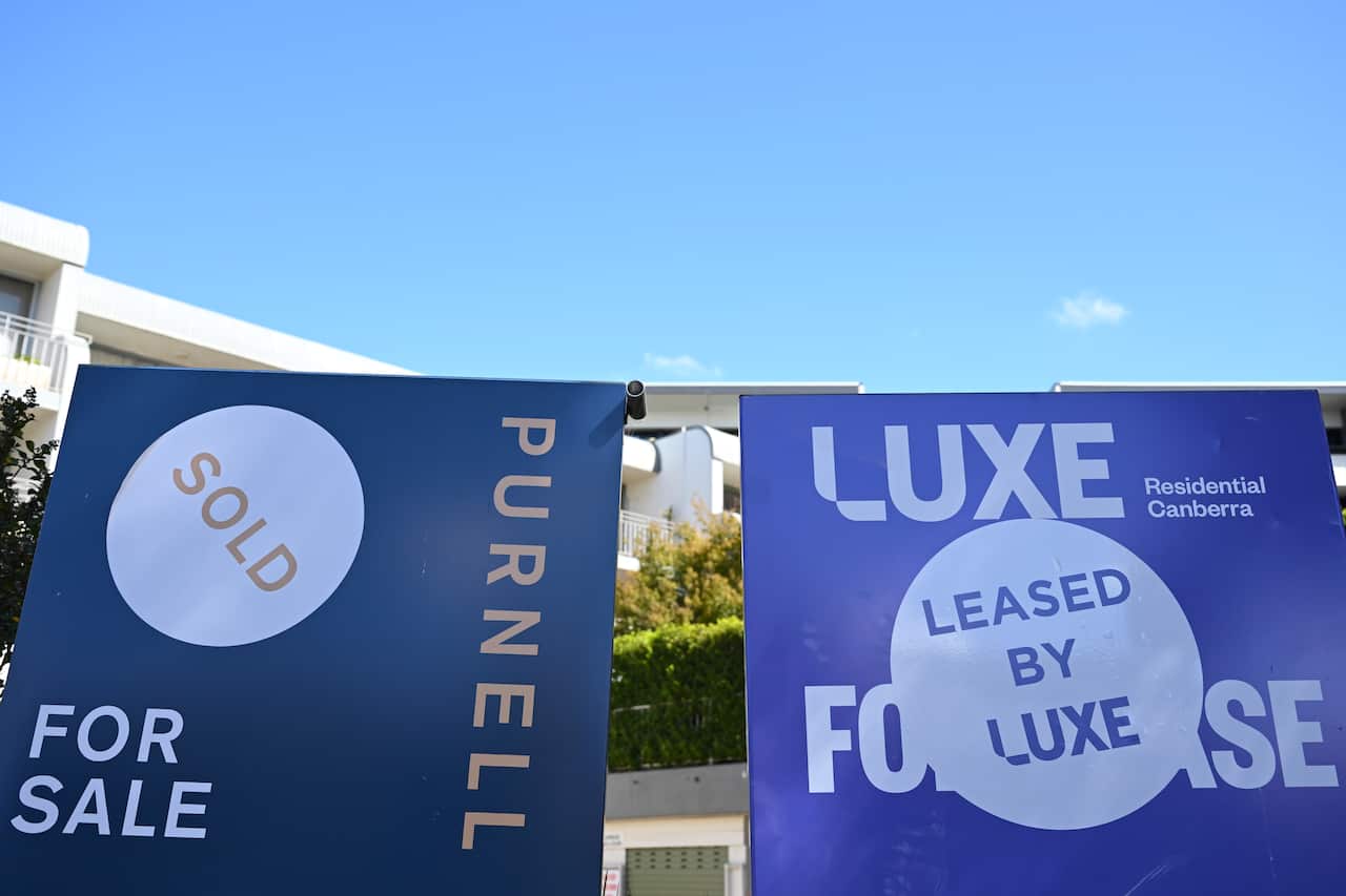 Two real estate signs in front of an apartment block. The sign on the left says "for sale" and the sign on the right says "leased".