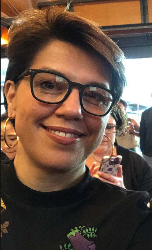 A woman with short dark hair and glasses smiling at the camera.