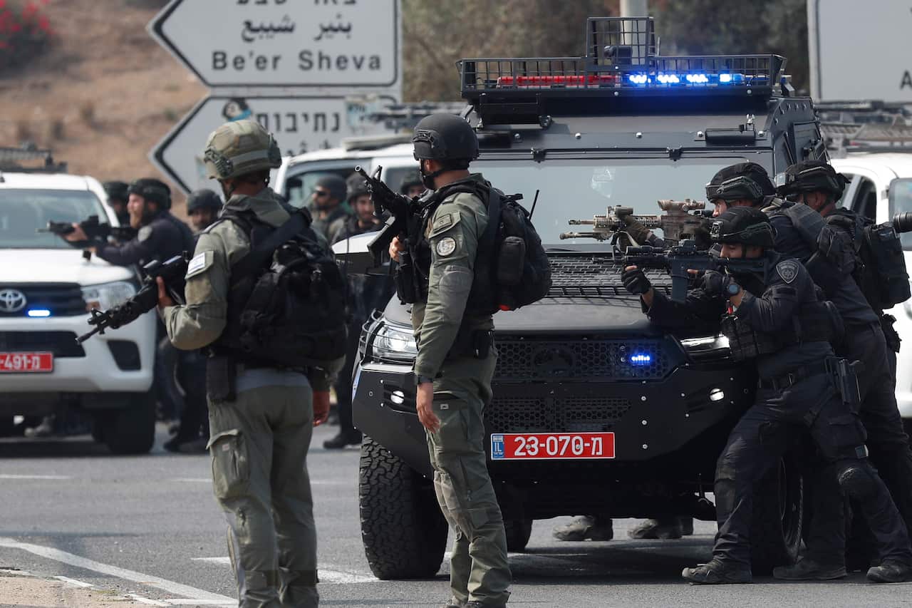 Israeli soldiers stand next to parked vehicles with their guns aimed.