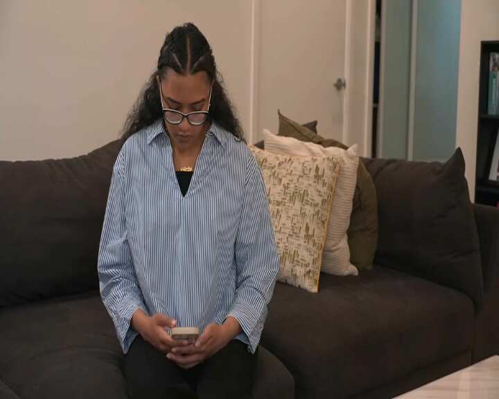 A woman in a striped shirt is looking down at her phone screen.