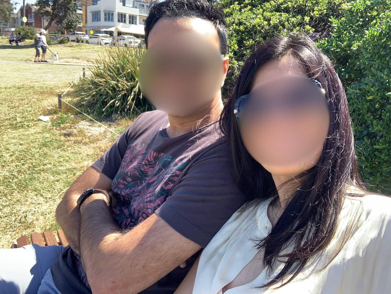 Two people whose faces have been blurred sit on a park bench.