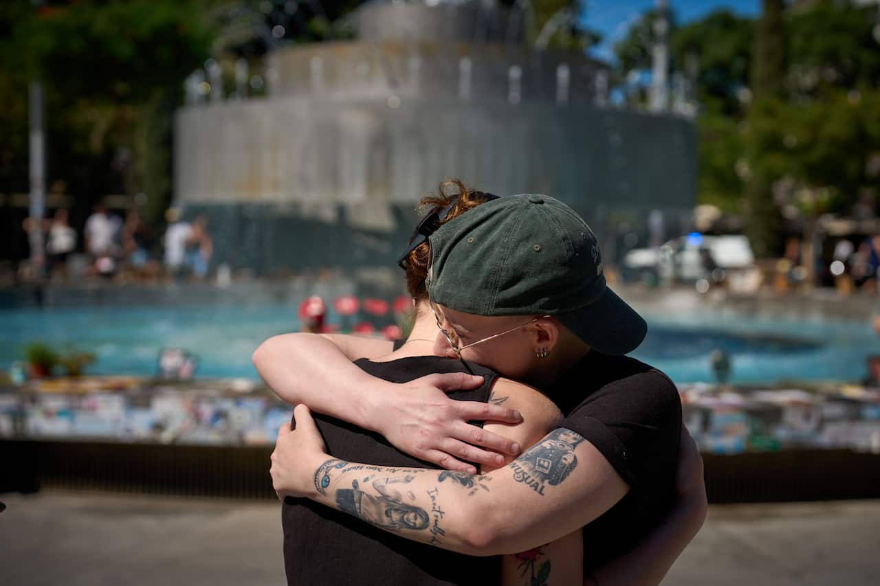 Two people embrace at a memorial for the October 7 victims beside a fountain in Tel Aviv.