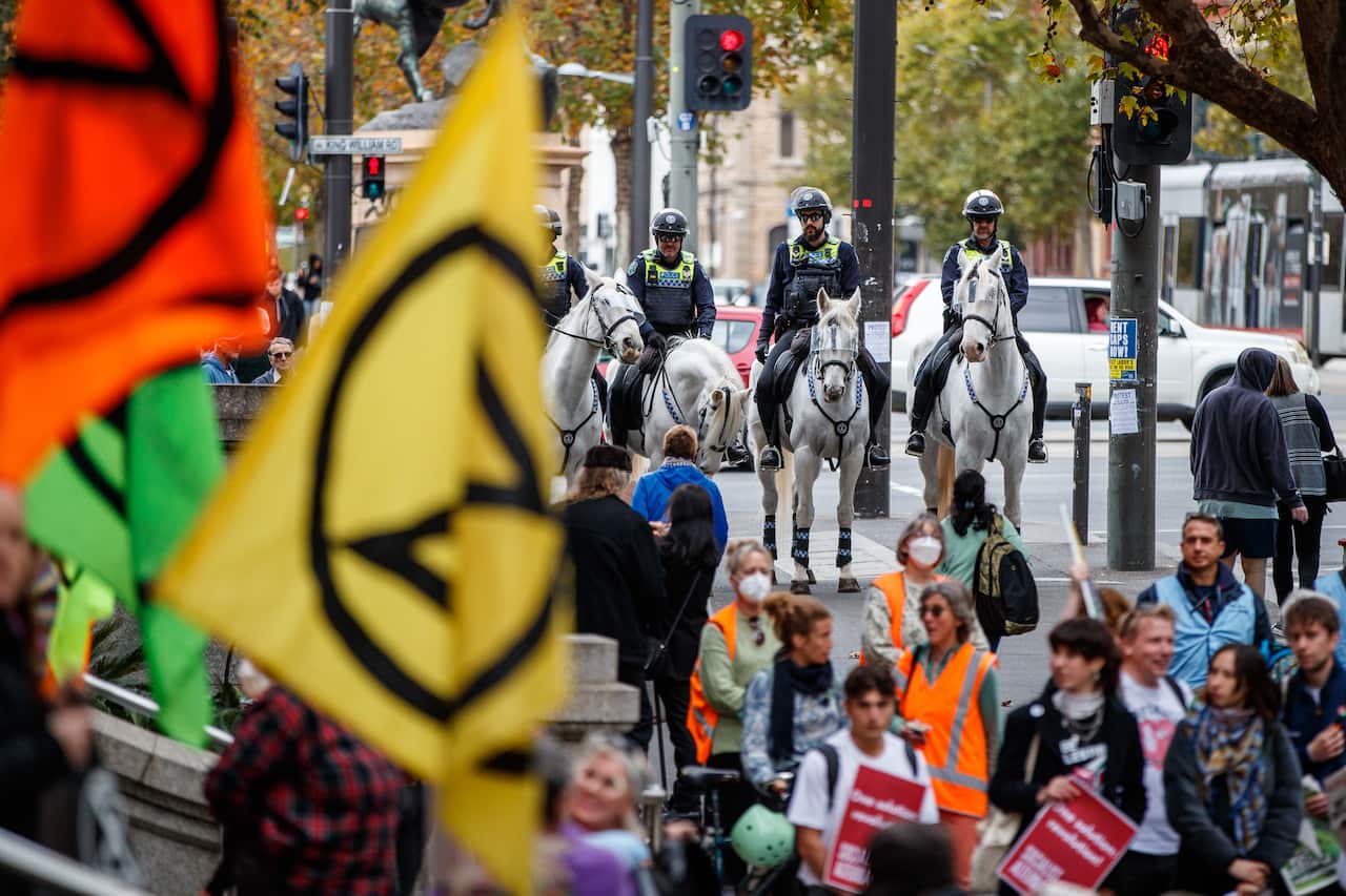 A group of climate protesters waving flags as police on horses watch in background.