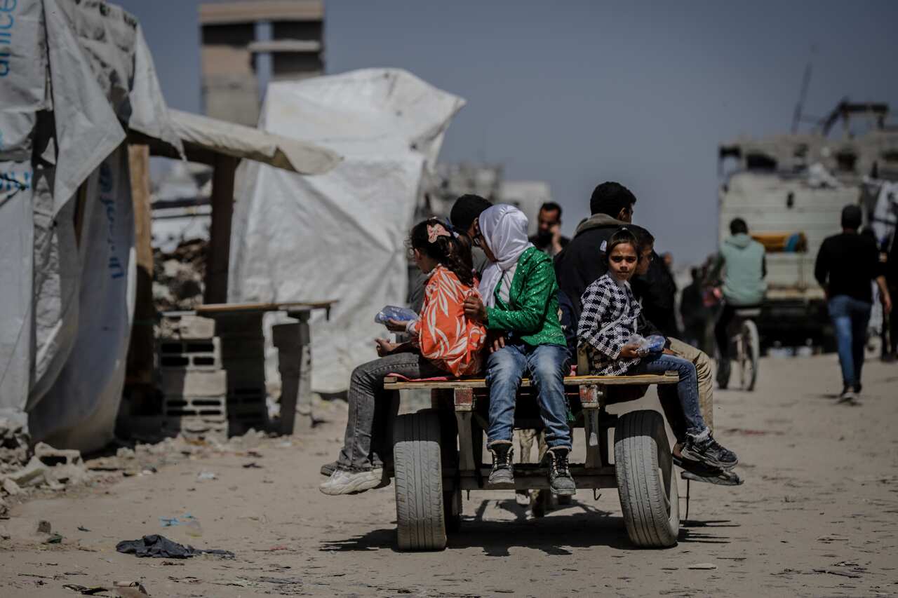 Children sit on the back of a cart, riding through tent camps.