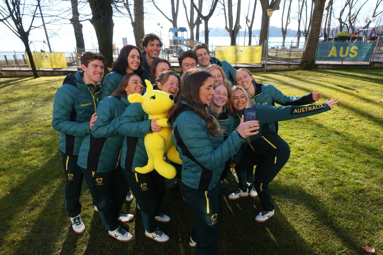 Australian athletes in green uniform pose for a group selfie on some grass outside