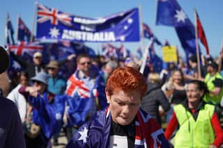 Pauline Hanson, draped in an Australian flag. She's in a crowd where many other people are wearing Australian flags. A large banner with the Australian flag reads "March for Australia".